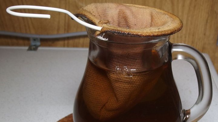 Ein Glas mit warmem Heiltee, der durch einen Stofffilter gezogen wird, steht auf einem Untersetzer in einer gem&uuml;tlichen K&uuml;che.