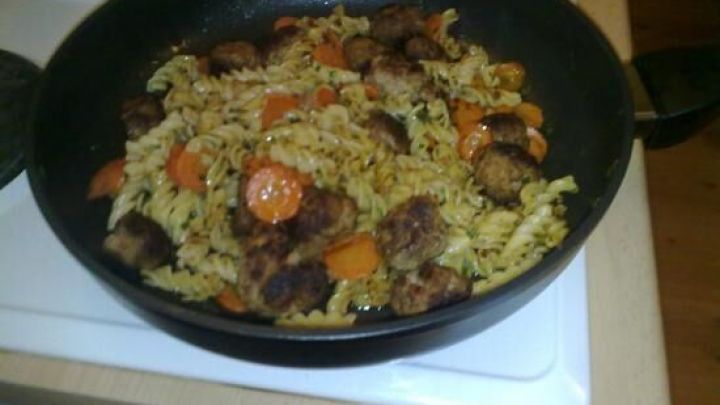 Eine bunte Nudelpfanne mit gebratenem Gem&uuml;se und Fleischst&uuml;cken wird in einer schwarzen Pfanne auf dem Herd serviert.