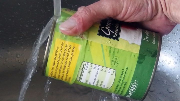 Eine Hand h&auml;lt eine Konservendose, w&auml;hrend sie unter flie&szlig;endem Wasser abgesp&uuml;lt wird, um Schmutz zu entfernen.