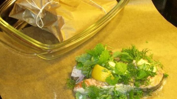 Lachskoteletts auf einem Kr&auml;uterbett mit Zitrone, vorbereitet in Pergamentpapier auf einer Backunterlage.