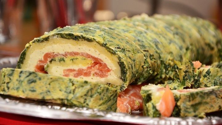 Eine Lachs-Spinatrolle liegt angeschnitten auf einem silbernen Tablett in einer festlichen Umgebung.