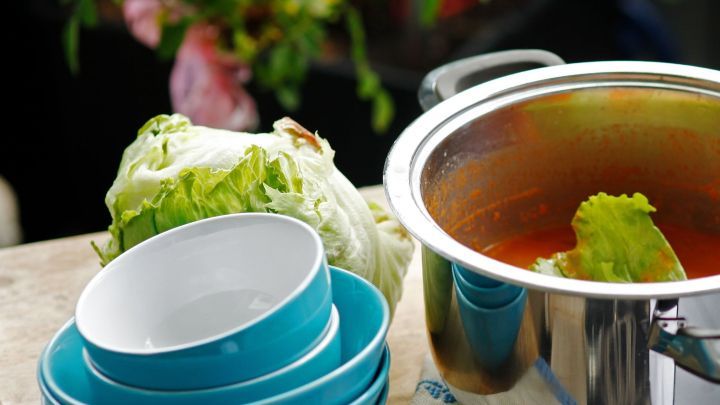 Ein Topf mit Suppe steht auf einem Tisch, w&auml;hrend Salatbl&auml;tter bereitliegen, um Fett zu entfernen, neben blauen Schalen.