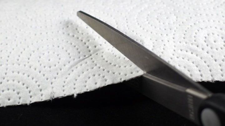 Eine Schere schneidet durch ein St&uuml;ck Haushaltspapier, um Material zu halbieren und Kosten zu sparen.