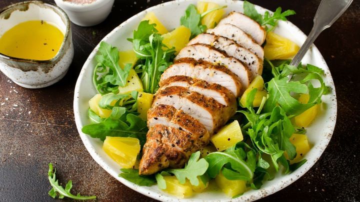 Eine Sch&uuml;ssel mit exotischem H&auml;hnchensalat enth&auml;lt gesunde Rucola-bl&auml;tter, St&uuml;cke von gegrilltem H&auml;hnchen und frische Ananas.