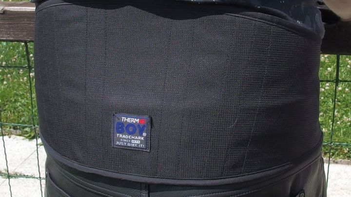 Ein Nierengurt w&auml;rmt den R&uuml;cken einer Person, die drau&szlig;en in einer gr&uuml;nen Umgebung steht, um sich vor der K&auml;lte zu sch&uuml;tzen.