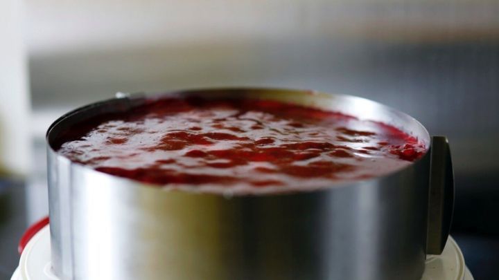 Ein Tortenring steht auf einer Torte mit roter F&uuml;llung, w&auml;hrend er sich sanft von der Torte l&ouml;st in einer modernen K&uuml;che.