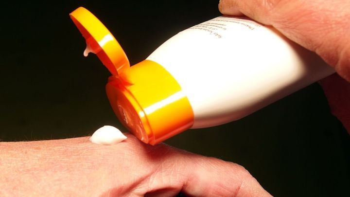 Eine Hand dr&uuml;ckt eine Flasche Sonnencreme aus, w&auml;hrend die andere Hand die Creme auf der Haut verteilt.