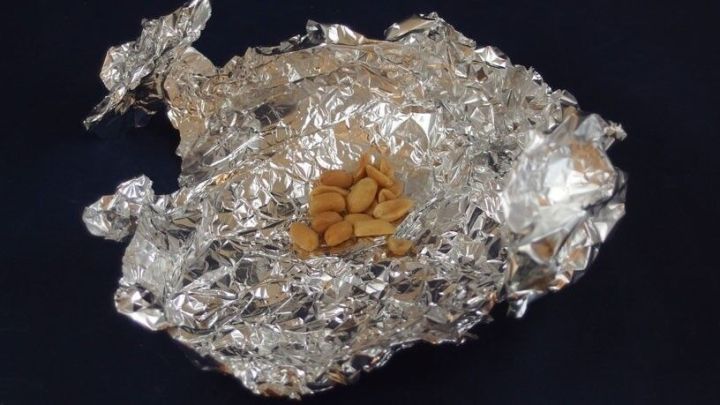 Alufolie umh&uuml;llt eine kleine Menge N&uuml;sse, die darin platziert sind, auf einem dunklen Hintergrund.