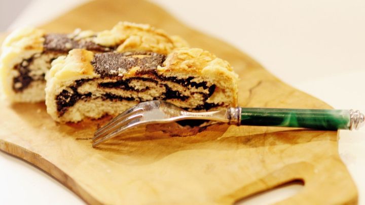 Ein Hefekranz mit Poppy-Filling liegt auf einem Holzbrett, neben einem eleganten Schneider, bereit zum Servieren.