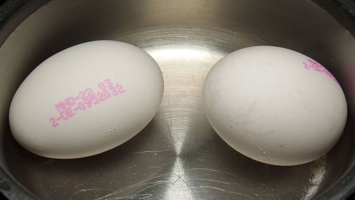 Zwei wei&szlig;e Eier liegen in einem Topf mit Wasser, w&auml;hrend sie im Kontext des Eierkochens ohne Verkalkung mit Essig vorbereitet werden.