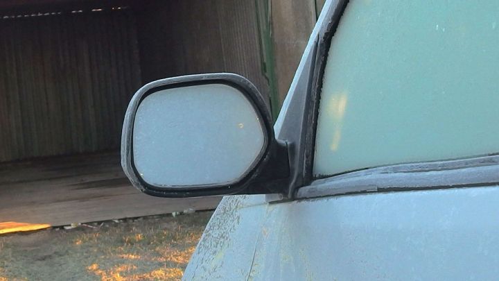 Ein vereister Auto-Au&szlig;enspiegel steht in einer schattigen Garage, umgeben von frostigem Wetter und morgenbl&auml;ulichem Licht.
