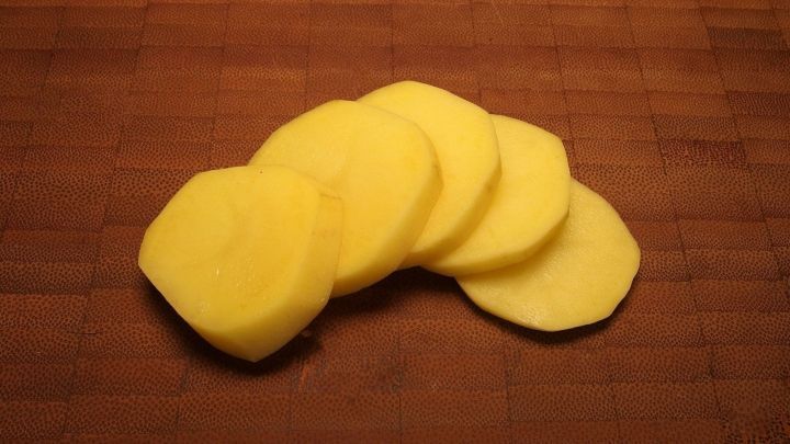 Scheiben einer Kartoffel liegen auf einem Holzbrett, bereit zur Verwendung in einer Gesichtsmaske f&uuml;r die Hautpflege.