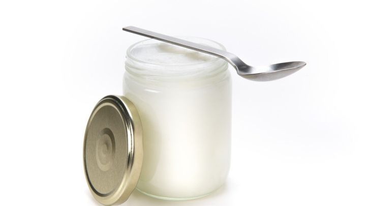 Ein Glas Kokos&ouml;l mit einem L&ouml;ffel steht auf einem Tisch, bereit zur Anwendung f&uuml;r die Hautpflege.