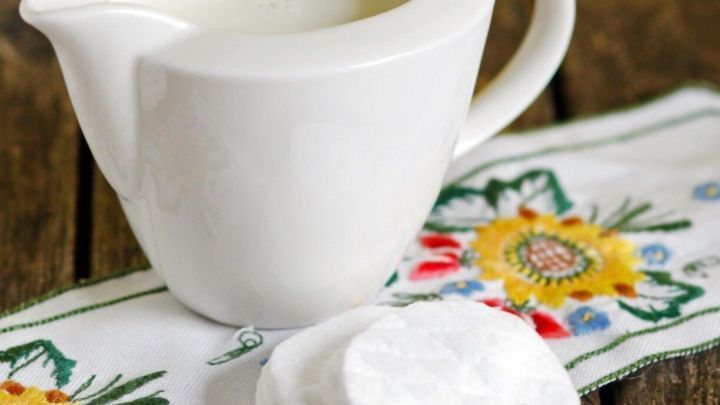 Eine wei&szlig;e Kanne mit Kondensmilch steht neben zwei Wattepads auf einem bunten, floral bestickten Tuch.
