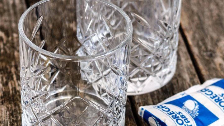 Klar strukturierte Wassergl&auml;ser stehen auf einem Holzuntergrund, neben ihnen liegen Reinigungstabletten zur Randentfernung.