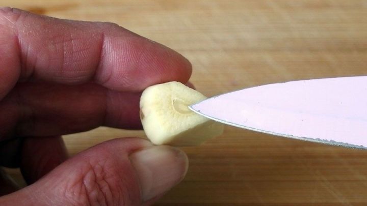Eine Hand h&auml;lt eine Knoblauchzehe, w&auml;hrend ein Messer an die Zehe angesetzt wird, um den unangenehmen Knoblauchgeruch zu reduzieren.