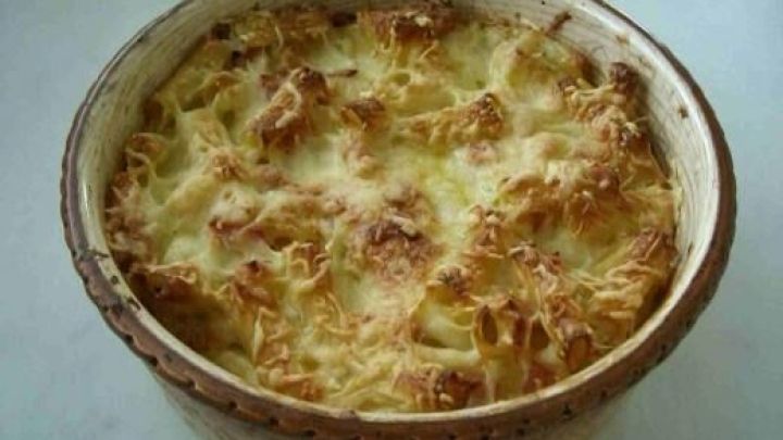 Ein Nudelauflauf mit goldbrauner Oberfl&auml;che wird in einer rustikalen Sch&uuml;ssel serviert, umgeben von wei&szlig;em Tischl&auml;ufer.