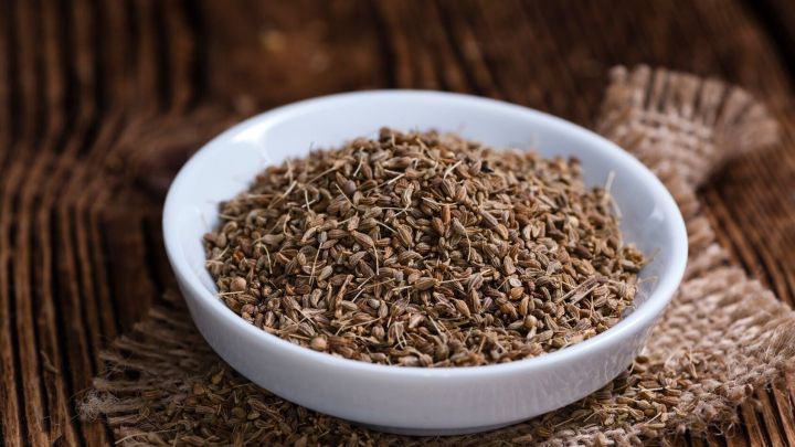 Eine wei&szlig;e Schale mit Anissamen steht auf einem rustikalen Holztisch, umgeben von einem groben Jutetuch.