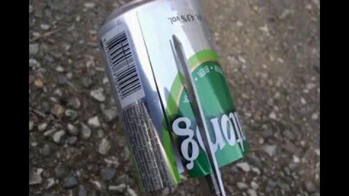 Eine Alu-Dose wird mit einer Schere geschnitten, um einen Recycling-Aschenbecher zu schaffen, liegend auf dem Boden.