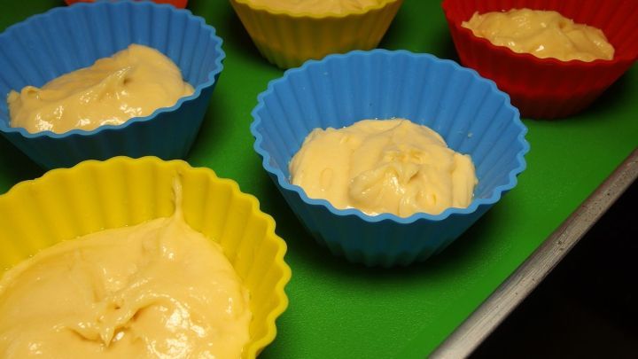 Bunte Silikonbackformen mit Teig stehen auf einer gr&uuml;nen Unterlage und warten darauf, in den Ofen transportiert zu werden.