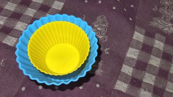 Zwei Silikonbackformen in Blau und Gelb stehen auf einem karierten Tisch, bereit zum Reinigen in Salzwasser.