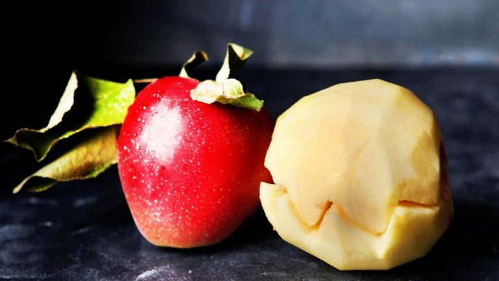 Ein roter Apfel steht neben einem gesch&auml;lten Apfel, der bereit ist, gegessen zu werden; beide liegen auf einer dunklen Fl&auml;che.