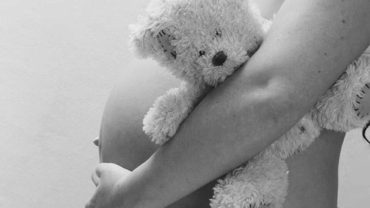 Eine schwangere Frau h&auml;lt einen Pl&uuml;schb&auml;ren liebevoll an ihrem Bauch, symbolisiert die Geburtsvorbereitung in einem ruhigen Umfeld.