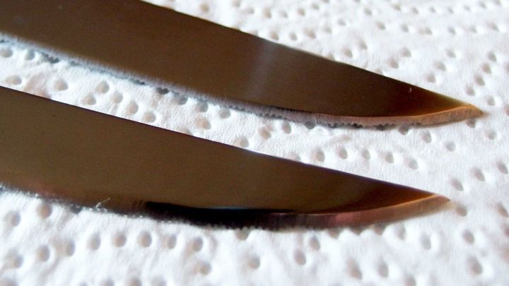 Zwei dunkle Messerschneiden liegen auf einem wei&szlig;en, strukturierten Tuch und reflektieren das Licht sanft.