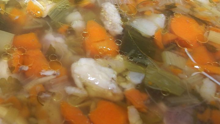 Bunte St&uuml;cke von Gem&uuml;se schwimmen in der Br&uuml;he und vermischen sich in einem Topf, der auf einem Herd steht.