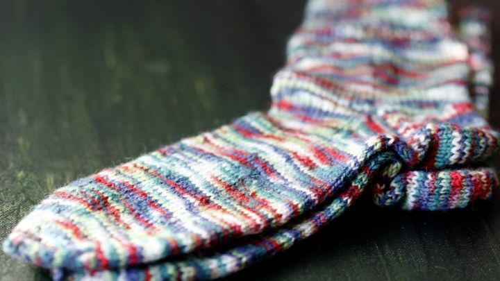 Bunte, gestrickte Socken liegen ordentlich auf einer dunklen Holzoberfl&auml;che, ideal f&uuml;r das Socken stricken.