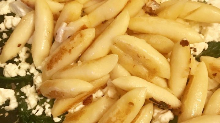 Schupfnudeln braten in einer Pfanne mit Spinat und Feta, goldbraun und knusprig gebraten, auf einem Herd.