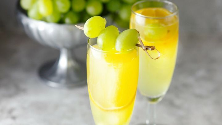 Zwei Gl&auml;ser gef&uuml;llt mit einem sprudelnden Getr&auml;nk aus Traubensaft und Ginger Ale stehen dekorativ vor einer Sch&uuml;ssel mit gr&uuml;nen Trauben.