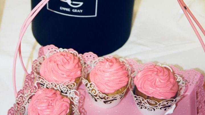 Eine schwarze Box enth&auml;lt k&uuml;nstliche rosa Blumen und steht neben pink verzierten Cupcakes auf einem Tisch, ideal f&uuml;r frischgebackene Eltern.
