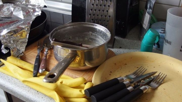 Auf der Arbeitsplatte stehen ein Kochtopf und ein Teller mit Besteck, w&auml;hrend Bananen und K&uuml;chenutensilien umherliegen.