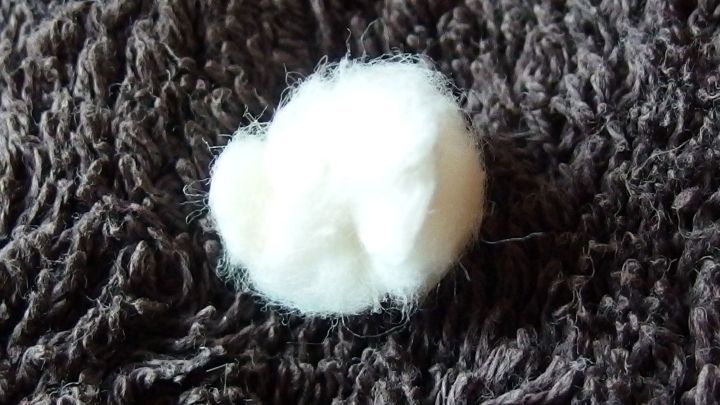 Wei&szlig;es Wattekn&uuml;llchen liegt auf einem dunklen, flauschigen Untergrund und k&ouml;nnte verwendet werden, um Ohren zu sch&uuml;tzen.