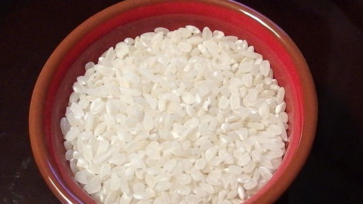 Ein roter Sch&uuml;ssel voll mit ungekochtem Reis steht auf einem dunklen Tisch, ideal f&uuml;r Reis-Fans auf der Suche nach Alternativen.