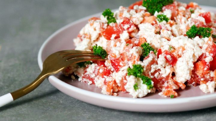 Ein frischer Sommersalat mit H&uuml;ttenk&auml;se und Tomaten wird auf einem Teller pr&auml;sentiert, garniert mit frischem Schnittlauch.