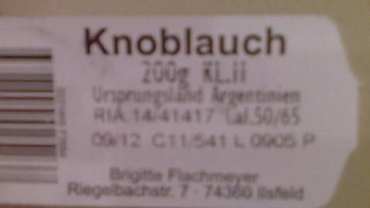 Ein Etikett zeigt frischen Knoblauch mit dem Mindesthaltbarkeitsdatum sowie Angaben zu Herkunft und Lagerung in einem Supermarkt.