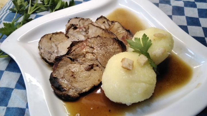 Auf einem Tellerrand liegt zart gegrillter Schweinebraten neben zwei Kartoffelkn&ouml;deln in k&ouml;stlicher Sauce.