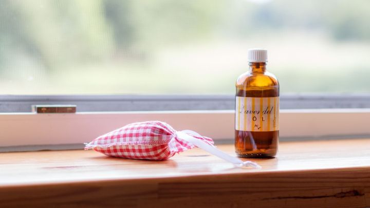 Eine braune Flasche und ein Lavendelkissen stehen auf einer Fensterbank, w&auml;hrend frische Luft von drau&szlig;en hereinkommt.