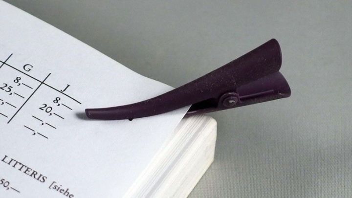 Eine Haarklemme sitzt als Lesezeichen auf einem aufgeschlagenen Buch, das auf einem neutralen Untergrund liegt.