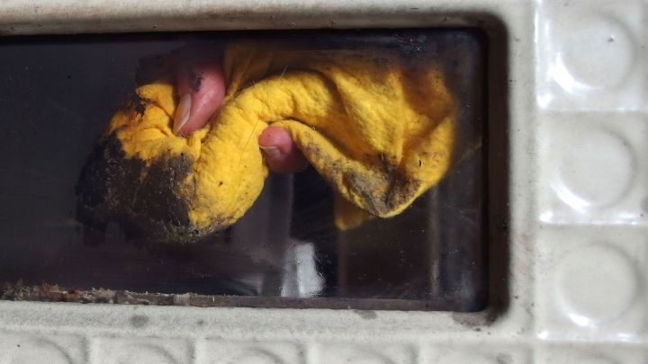 Ein gelbes Tuch wird zum Reinigen des Glasfensters eines Kaminofens verwendet, um Schmutz zu entfernen.