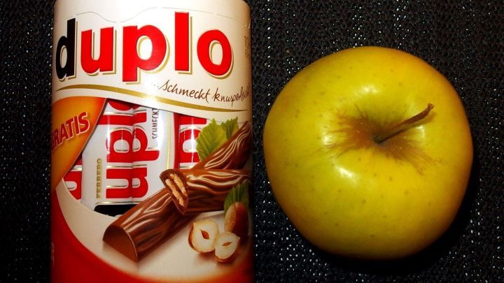 Ein Duppo-Riegel steht neben einem gr&uuml;nen Apfel auf einer schwarzen Oberfl&auml;che, die gesunde Wahl gegen den inneren Schweinehund.