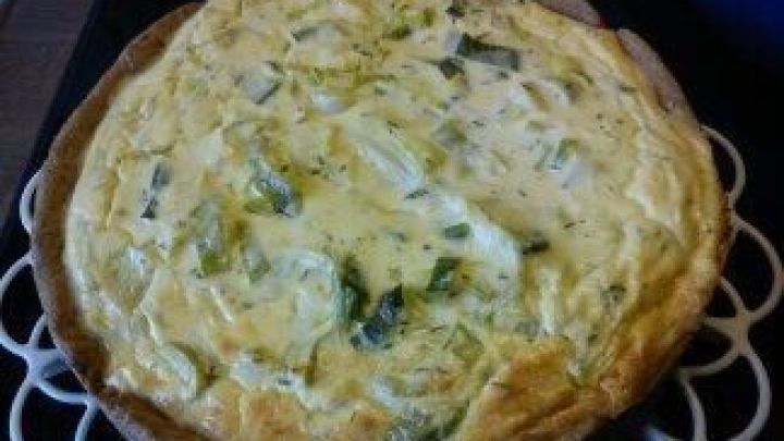 Ein goldbrauner Lauchkuchen mit Feta liegt auf einem wei&szlig;en Kuchengitter und wartet darauf, serviert zu werden.