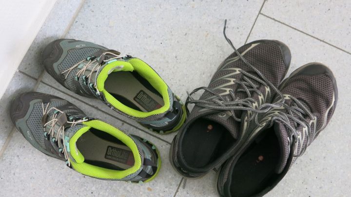 Zwei Paar Turnschuhe liegen auf grauen Fliesen nebeneinander; eines hat gr&uuml;ne Details, das andere ist schwarz.