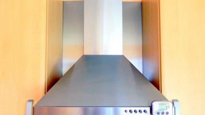 Die Abzugshaube gl&auml;nzt nach einer Reinigung mit Sp&uuml;lmittel und Wasser, eingebaut in eine moderne K&uuml;che mit Holzverkleidung.