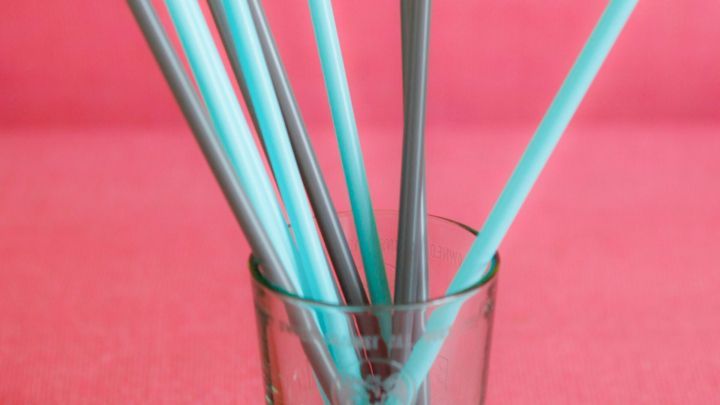 Bunte Trinkhalme stehen in einem transparenten Glas auf einem pinken Hintergrund und warten auf die n&auml;chste Verwendung.