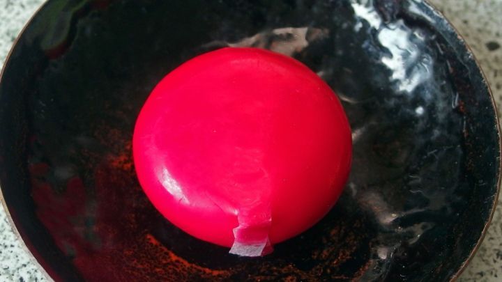 Rote Wachsh&uuml;lle liegt auf schwarzem Teller; diese umh&uuml;llt einen Mini-K&auml;se und bietet Potenzial zur Weiterverwertung.