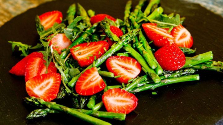 Frischer Spargel und saftige Erdbeeren liegen bunt auf einem schwarzen Teller und bilden einen ansprechenden Salat.