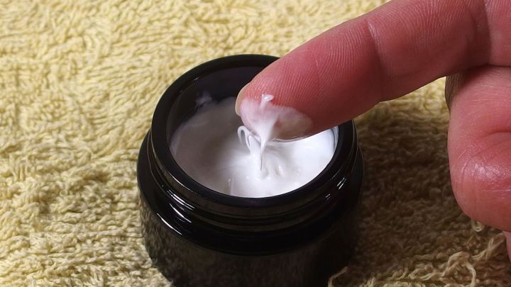 Ein Finger taucht in ein schwarzes Glasgef&auml;&szlig; mit pflegendem Lippenbalsam, um es auf eine sanfte Weise aufzutragen.